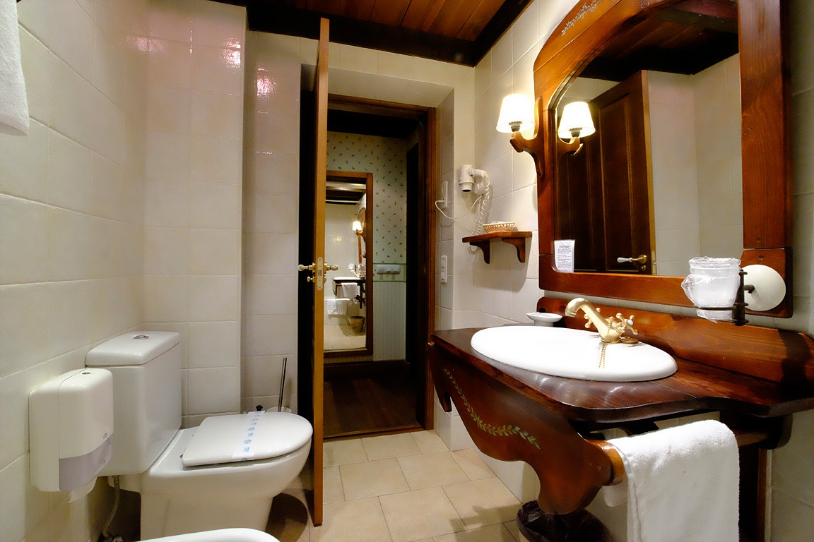 Baño con inodoro blanco, lavabo, espejo y puerta abierta a otra habitación.