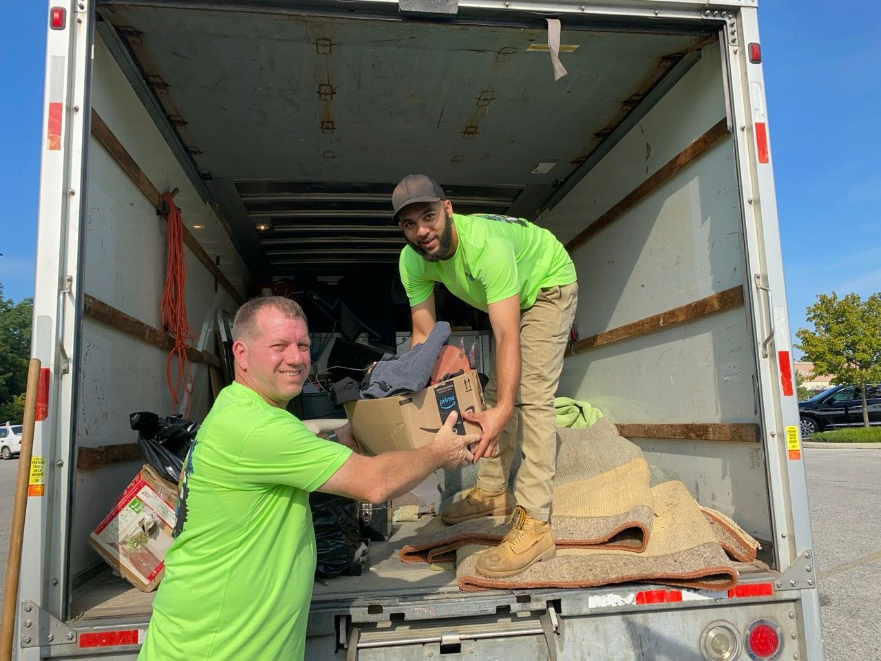 Two men in green shirts are standing in the back of a truck.