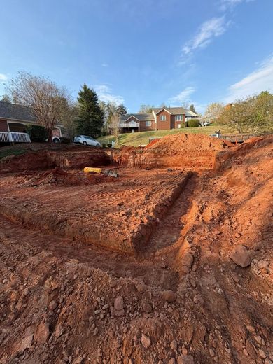 Red clay excavation site with a steep cut beside houses under a blue sky