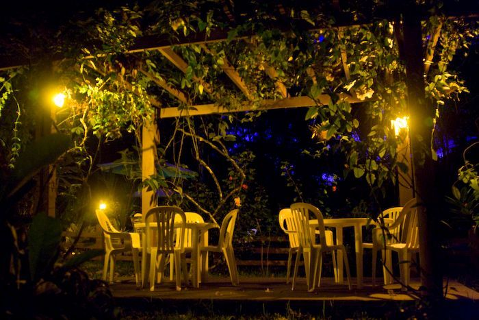 A group of tables and chairs under a pergola at night.