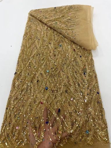 A person is holding a piece of gold lace fabric.