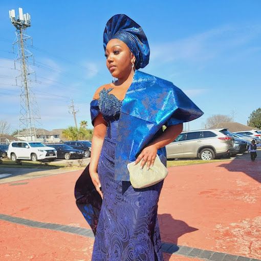 A woman in a blue dress and turban is standing in a parking lot.