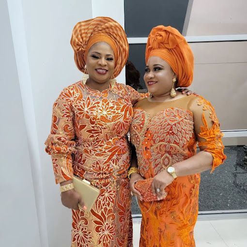 Two women in orange dresses and turbans are posing for a picture.