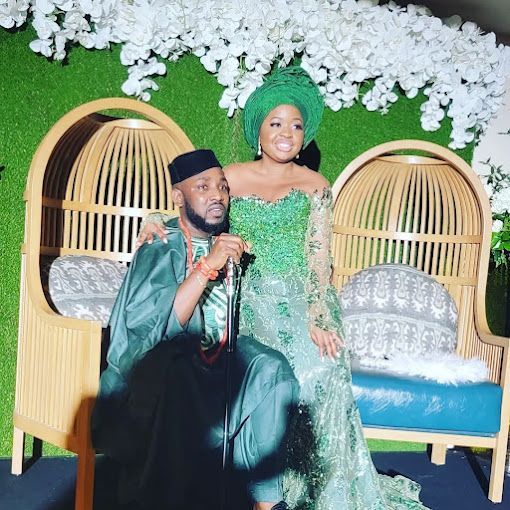 A man and a woman are sitting next to each other on a couch . the woman is wearing a green dress.