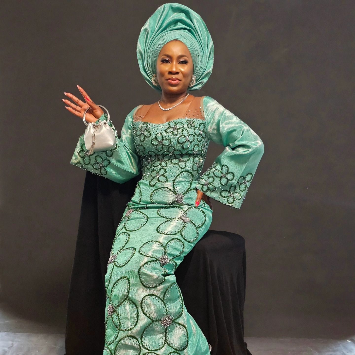 A woman in a green dress and turban is sitting on a chair.