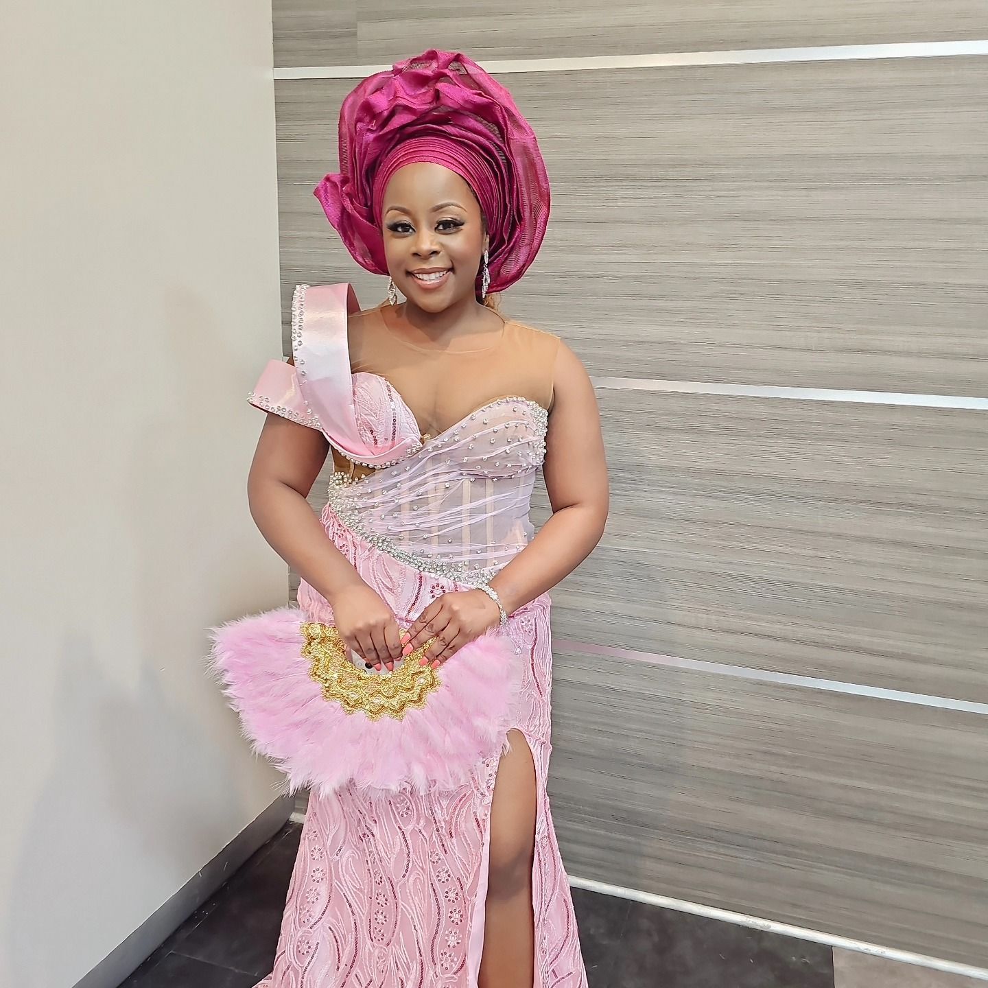 A woman in a pink dress is holding a fan and smiling.