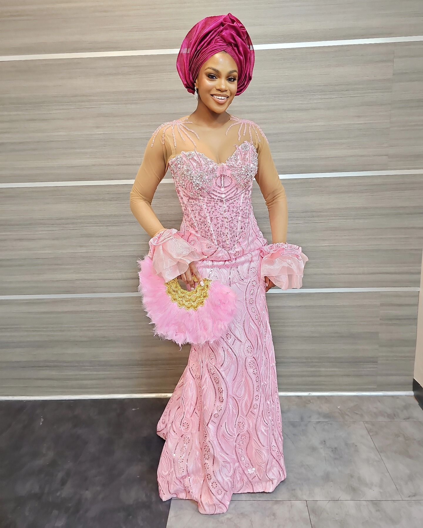 A woman is wearing a pink lace dress and holding a fan.
