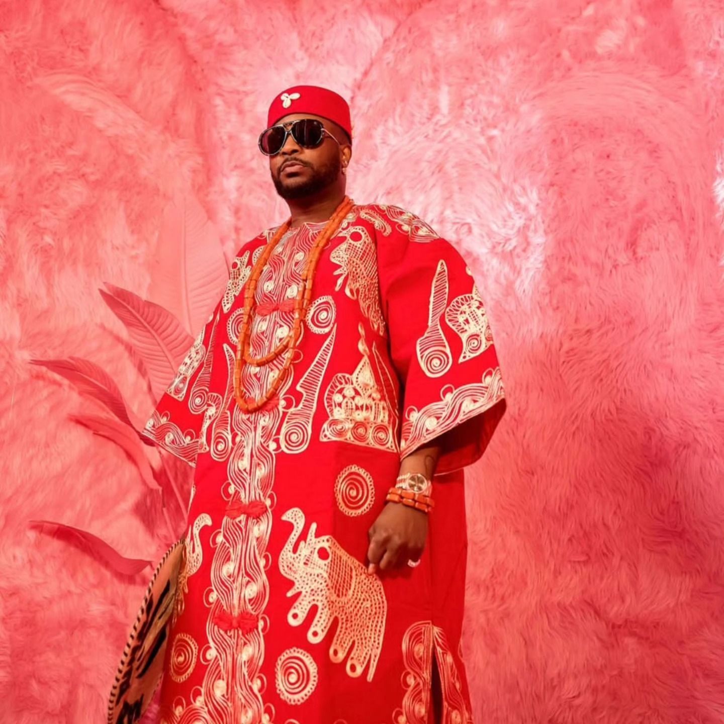 A man in a red and gold dress is standing in front of a pink wall.