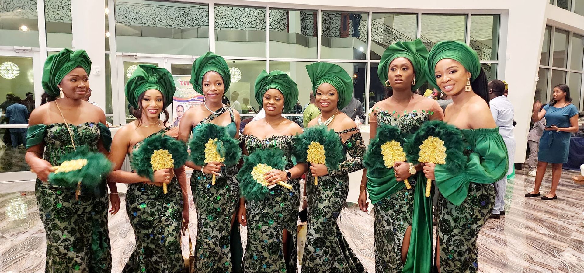 A group of women in green dresses are standing next to each other holding fans.