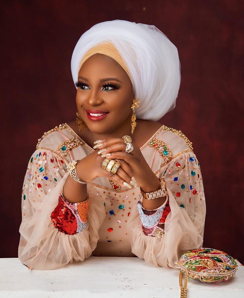 A woman wearing a white turban is sitting at a table with her hands folded.