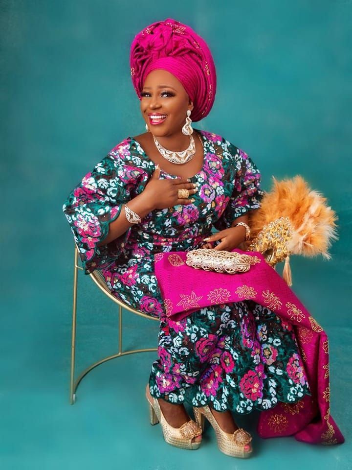 A woman in a floral dress is sitting on a chair holding a fan.