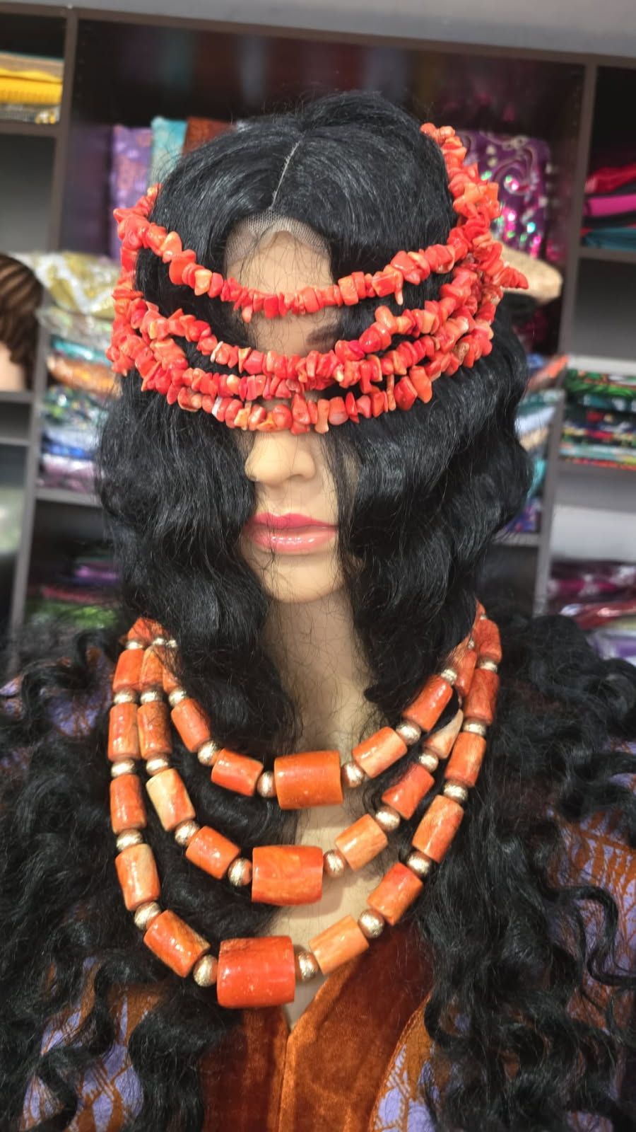 A mannequin wearing a wig and a necklace of orange beads.