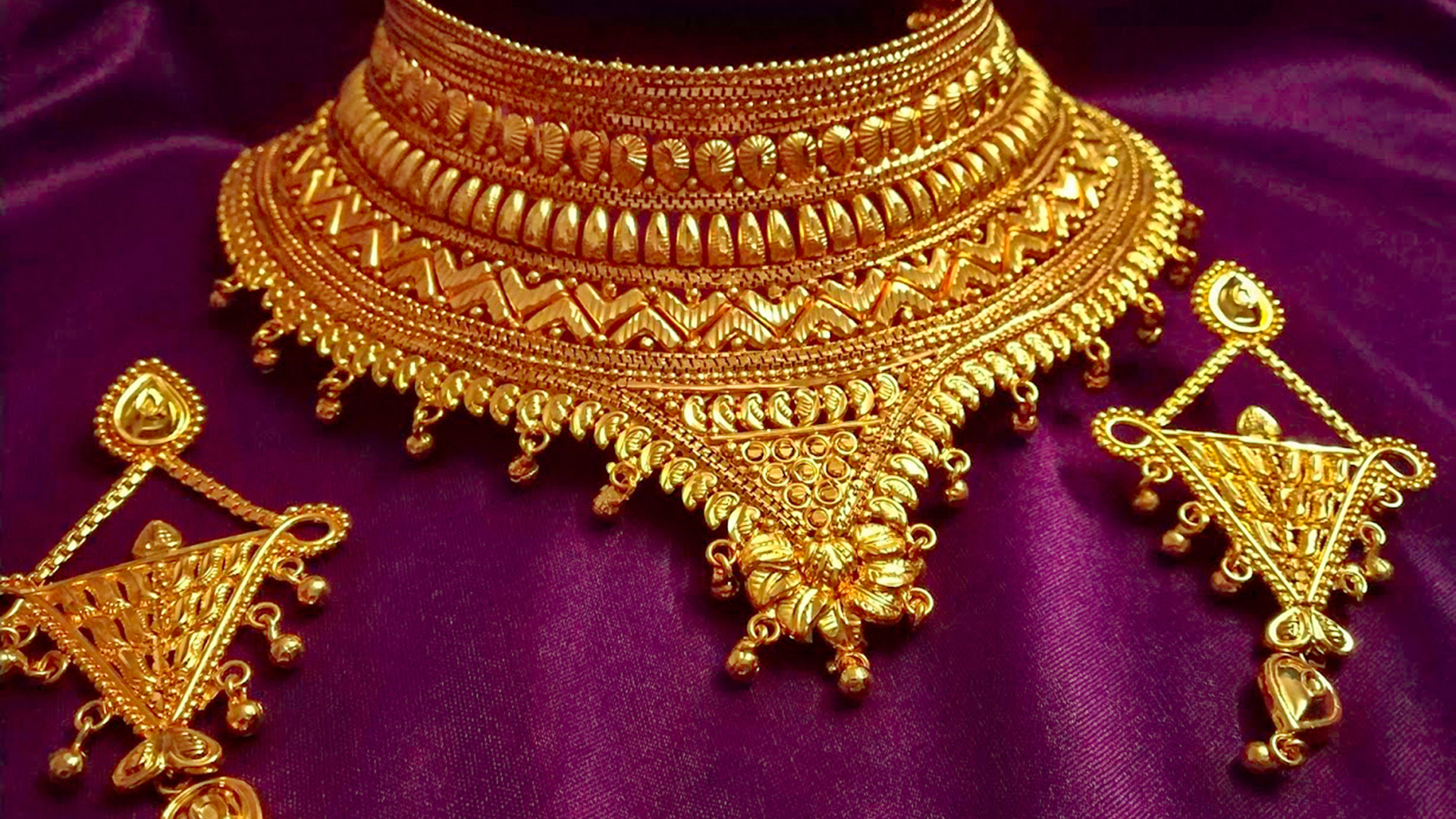 A gold necklace and earring set on a purple cloth