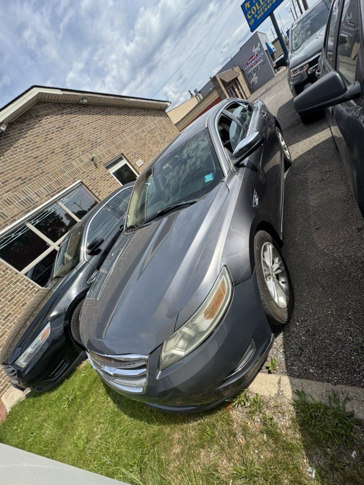 Gray sedan parked on grass next to a brick building.