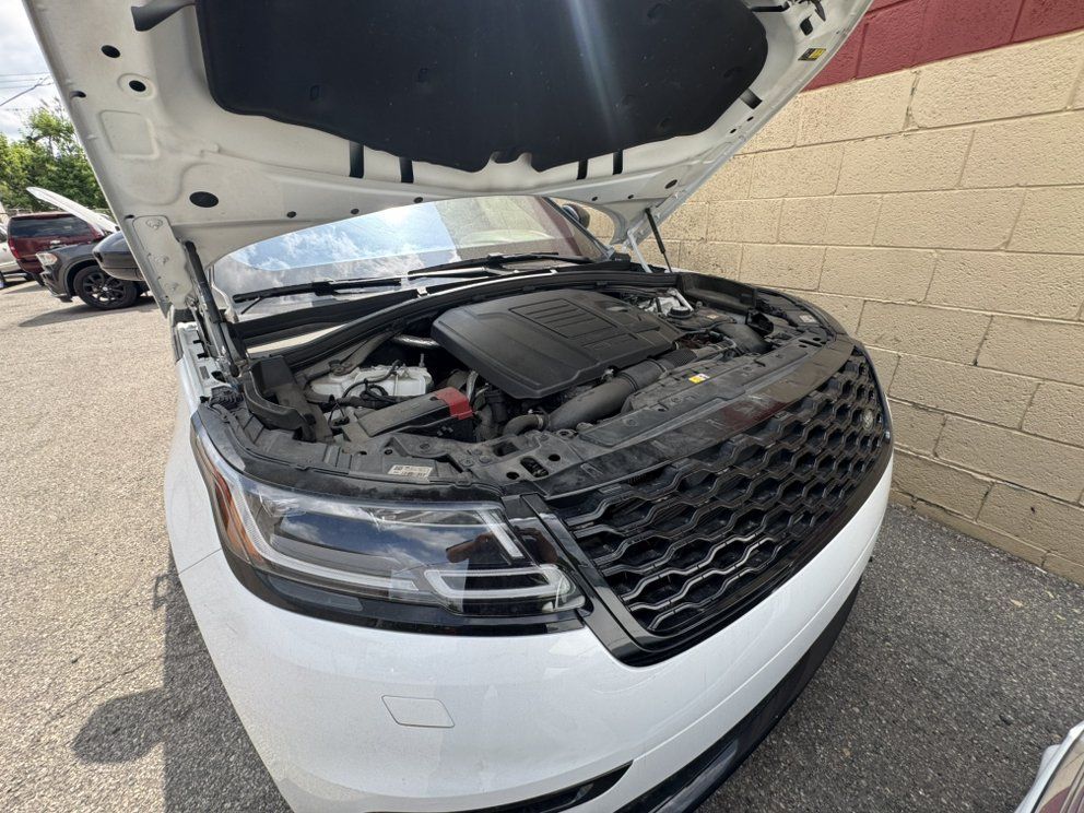 White SUV with hood open, parked near a red brick wall. Engine visible, grill in foreground.