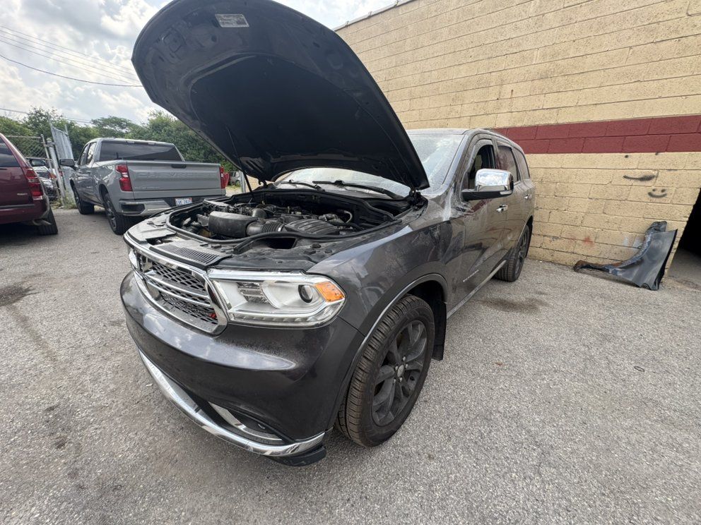 Gray Dodge Durango SUV with the hood open, parked next to a brick building.