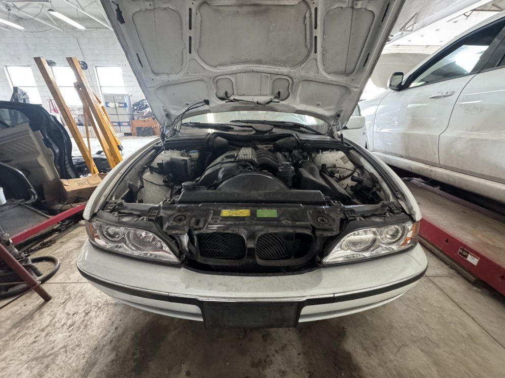White BMW with the hood open in a repair shop, showing the engine.