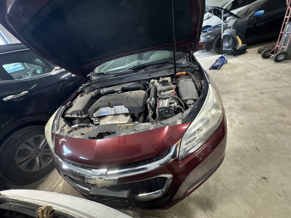 Red Chevrolet Malibu with hood open in a garage, revealing the engine.