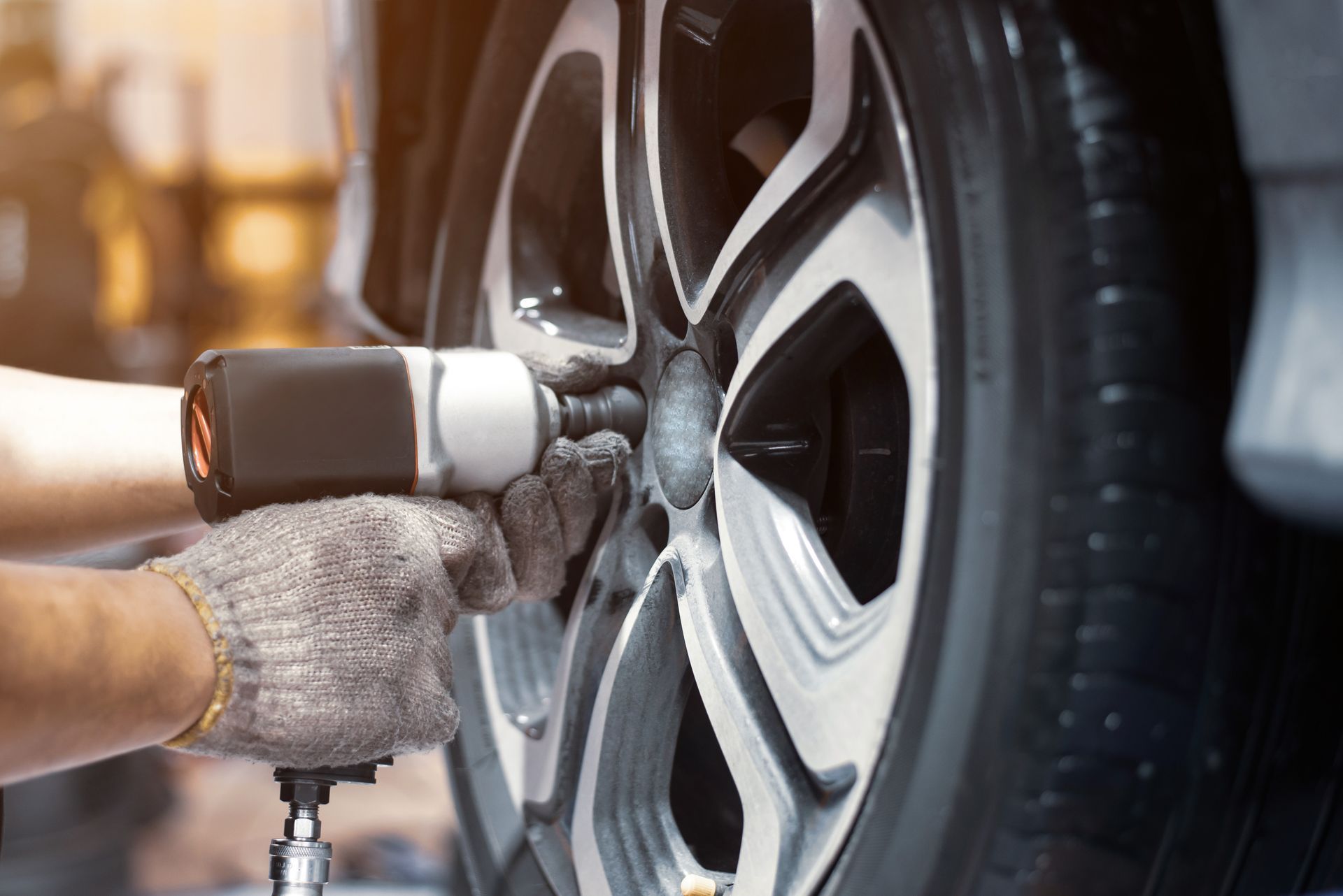 Mechanic using an impact wrench to tighten lug nuts on a car's tire.