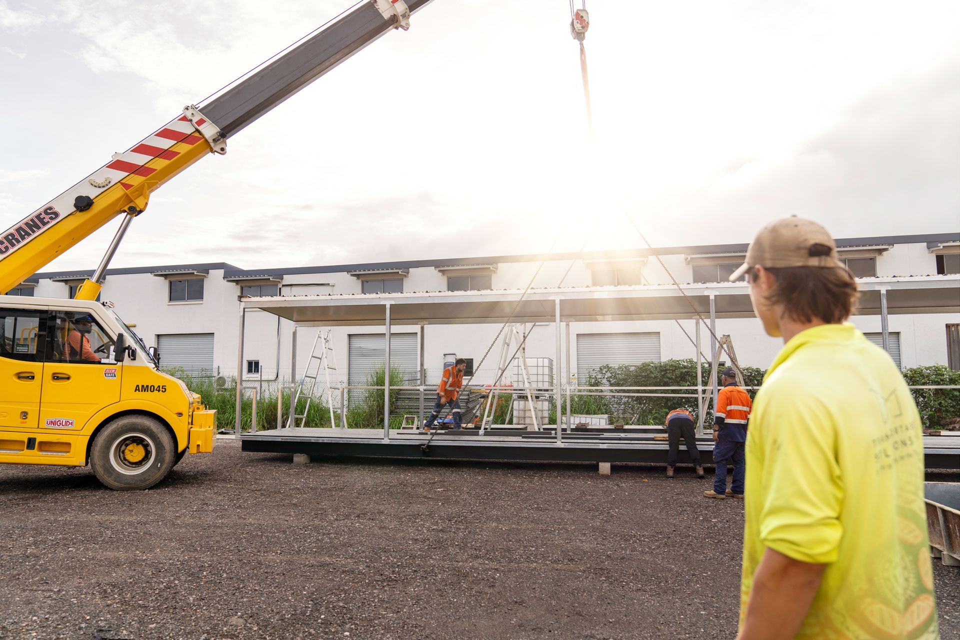 A man in a yellow shirt is standing in front of a yellow crane.