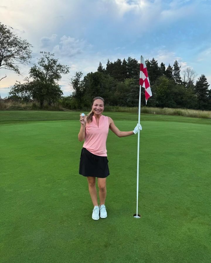 A woman is standing on a golf course holding a golf club and a golf ball.