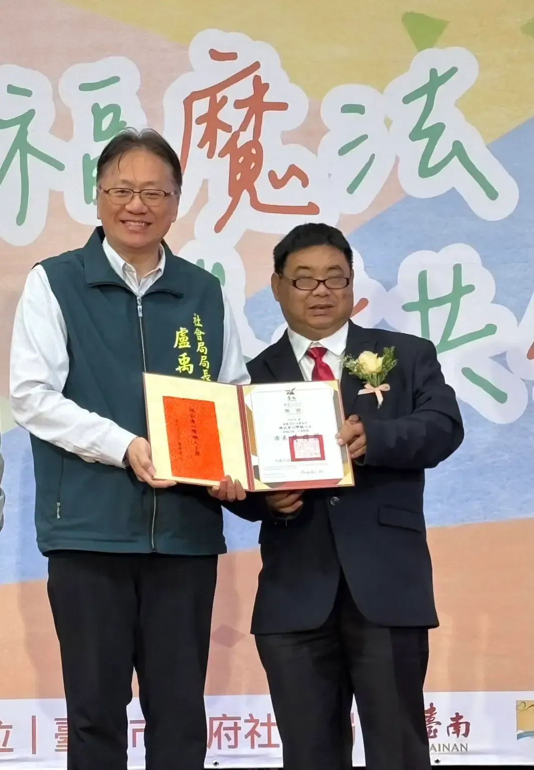 兩名男子在戶外活動中手捧獎品,面帶微笑,背景是中文。