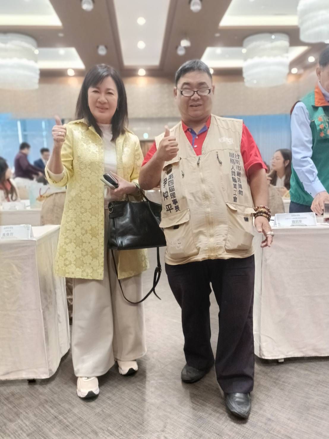 在一次活動中,身穿黃色外套的女子和身穿背心的男子都豎起大拇指。