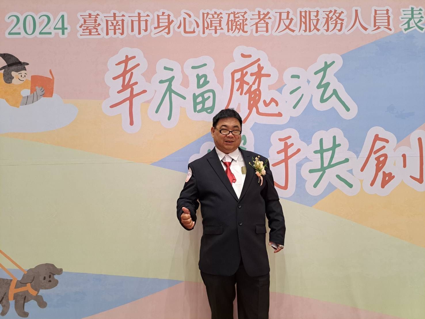 在台南市的一場活動中,一名身著西裝的男子微笑著站在寫有中文的布條前擺姿勢。