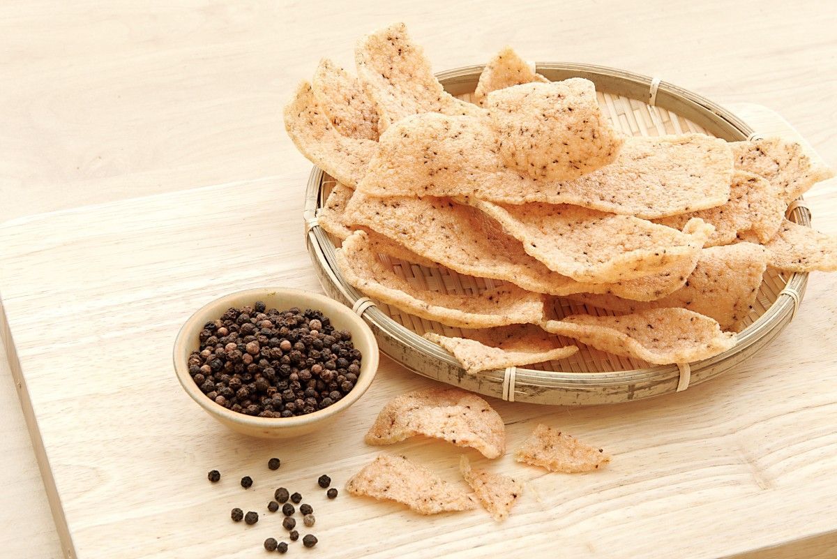 木質表面上，一籃蝦片旁邊放著煮熟的蝦子。