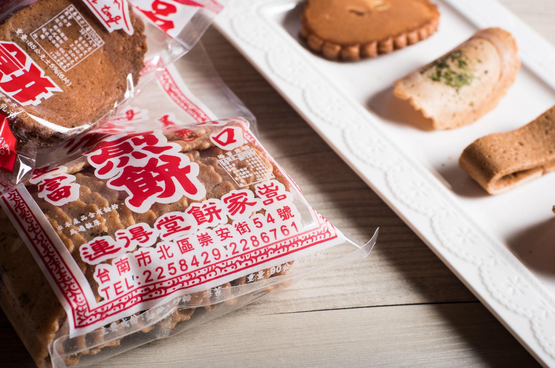 白色盤子上擺放著各種酥脆的烘焙小吃，有捲狀的，也有長方形的，上面有深色斑點。