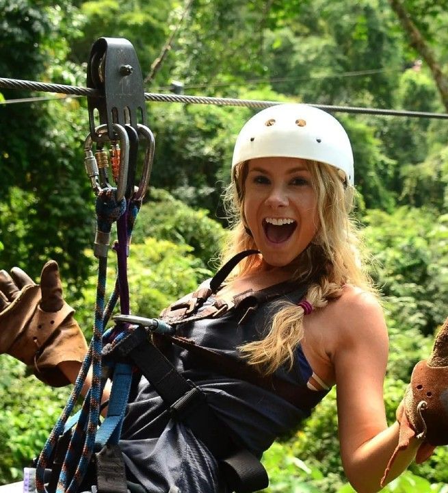 A woman wearing a white helmet is riding a zip line