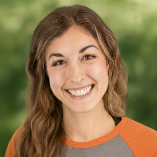 Woman with long wavy brown hair smiles at the camera, wearing an orange and gray shirt. Green background.