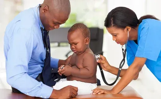 A baby is being examined by a doctor and nurse with a stethoscope.