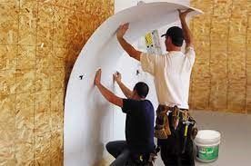Two men are working on a wall in a room.