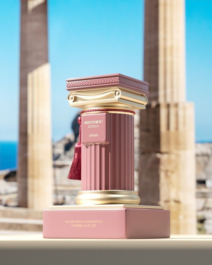 Frasco de perfume rosa con detalles dorados y borla, decorado con estatuas clásicas.