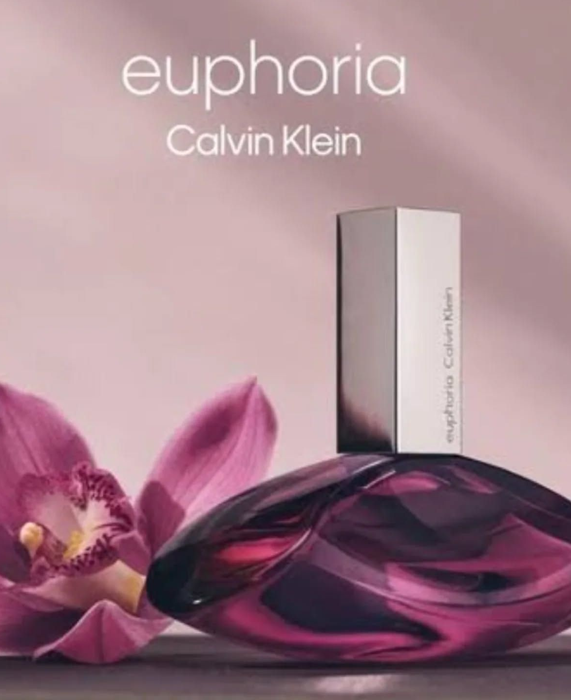 Frasco de perfume Calvin Klein Euphoria con flor de orquídea sobre fondo rosa.