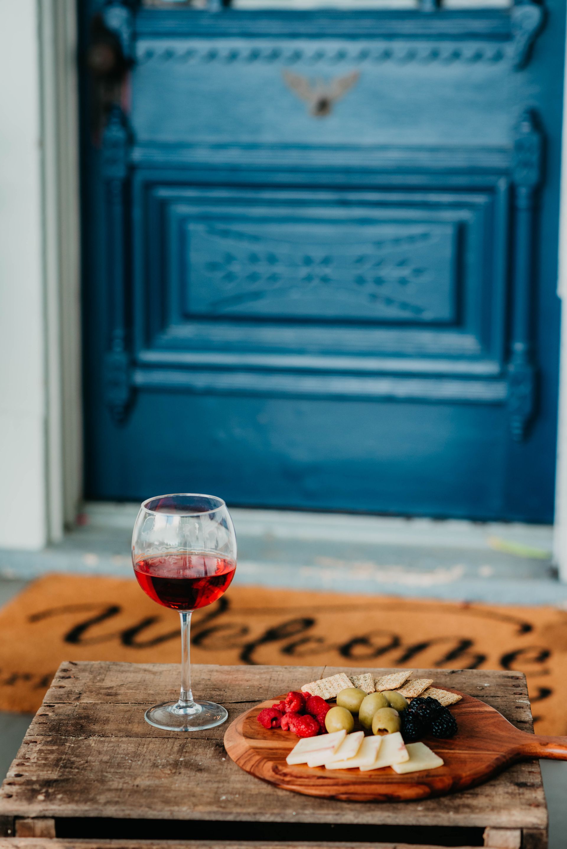 A glass of wine is sitting on a wooden table next to a welcome mat.