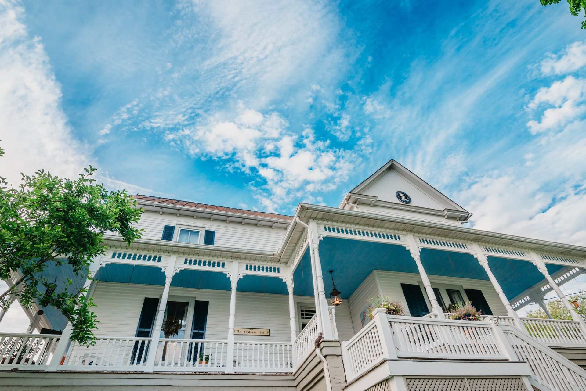 A large white house with a blue porch and a blue sky in the background.