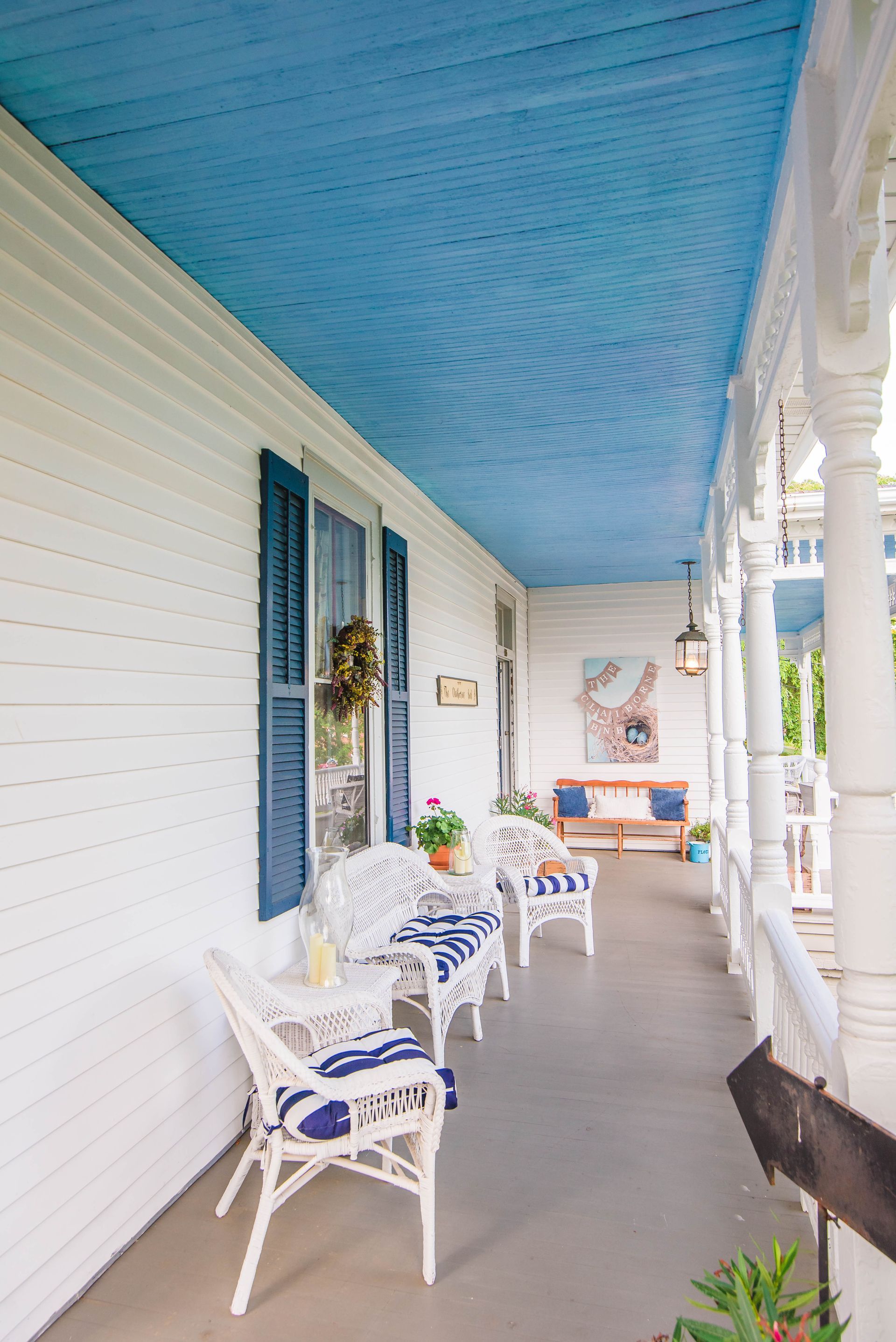 A porch with a blue ceiling and white furniture.