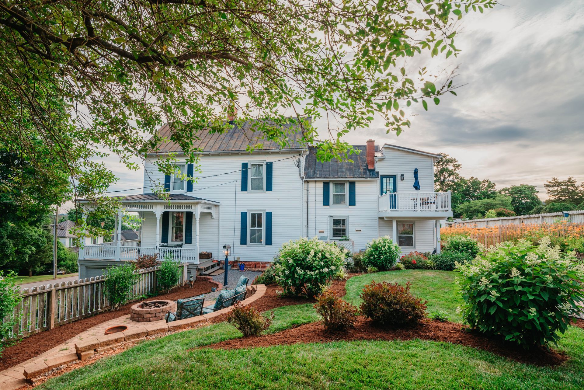 A large white house with blue shutters is sitting on top of a lush green lawn.