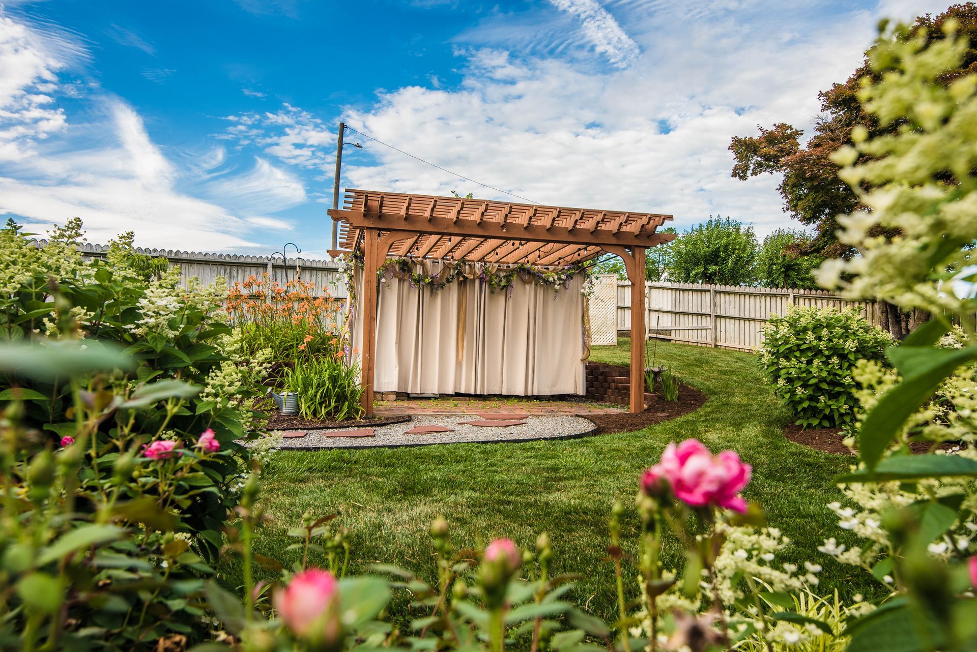 There is a pergola in the middle of a garden surrounded by flowers.