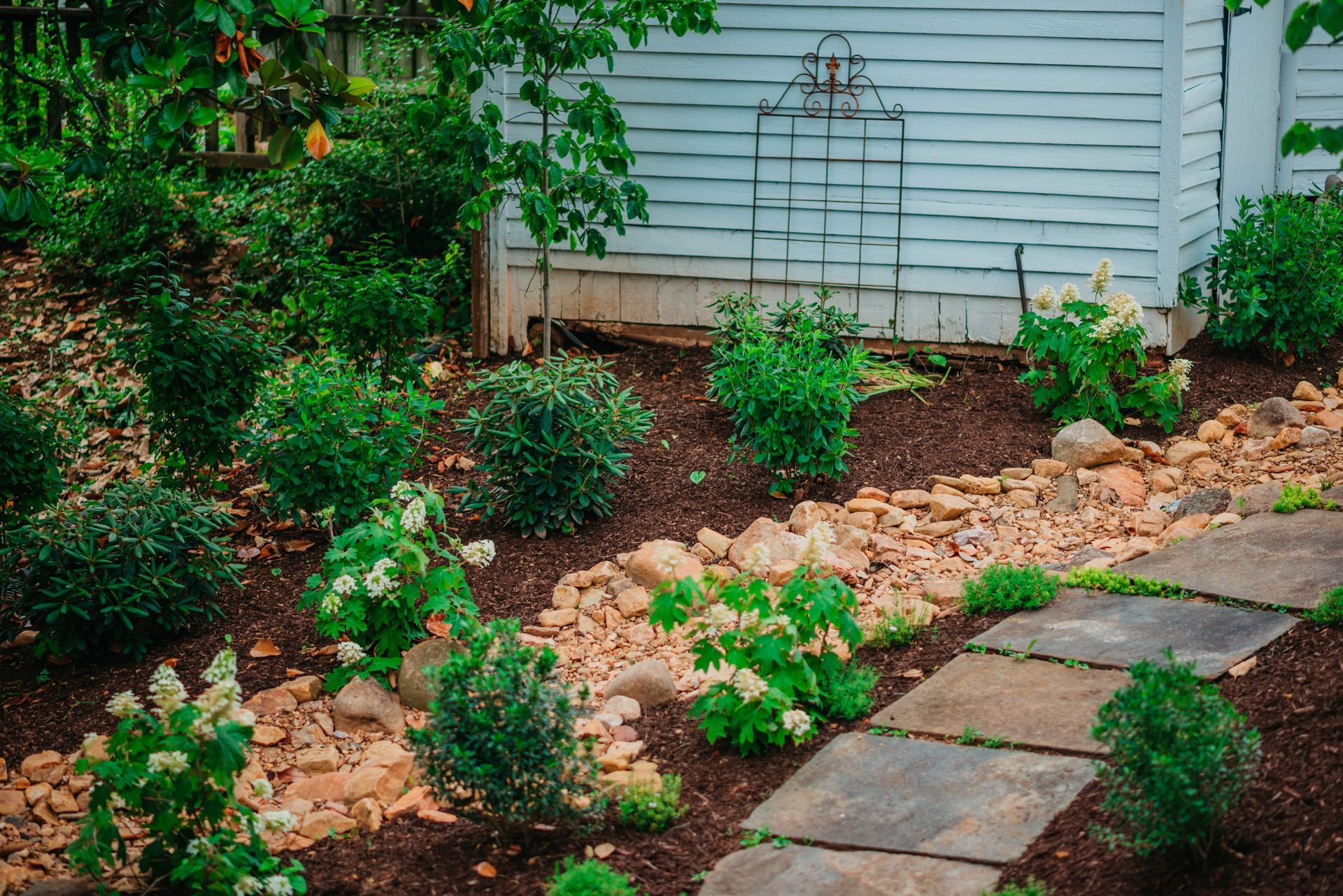A stone walkway in a garden next to a white house.