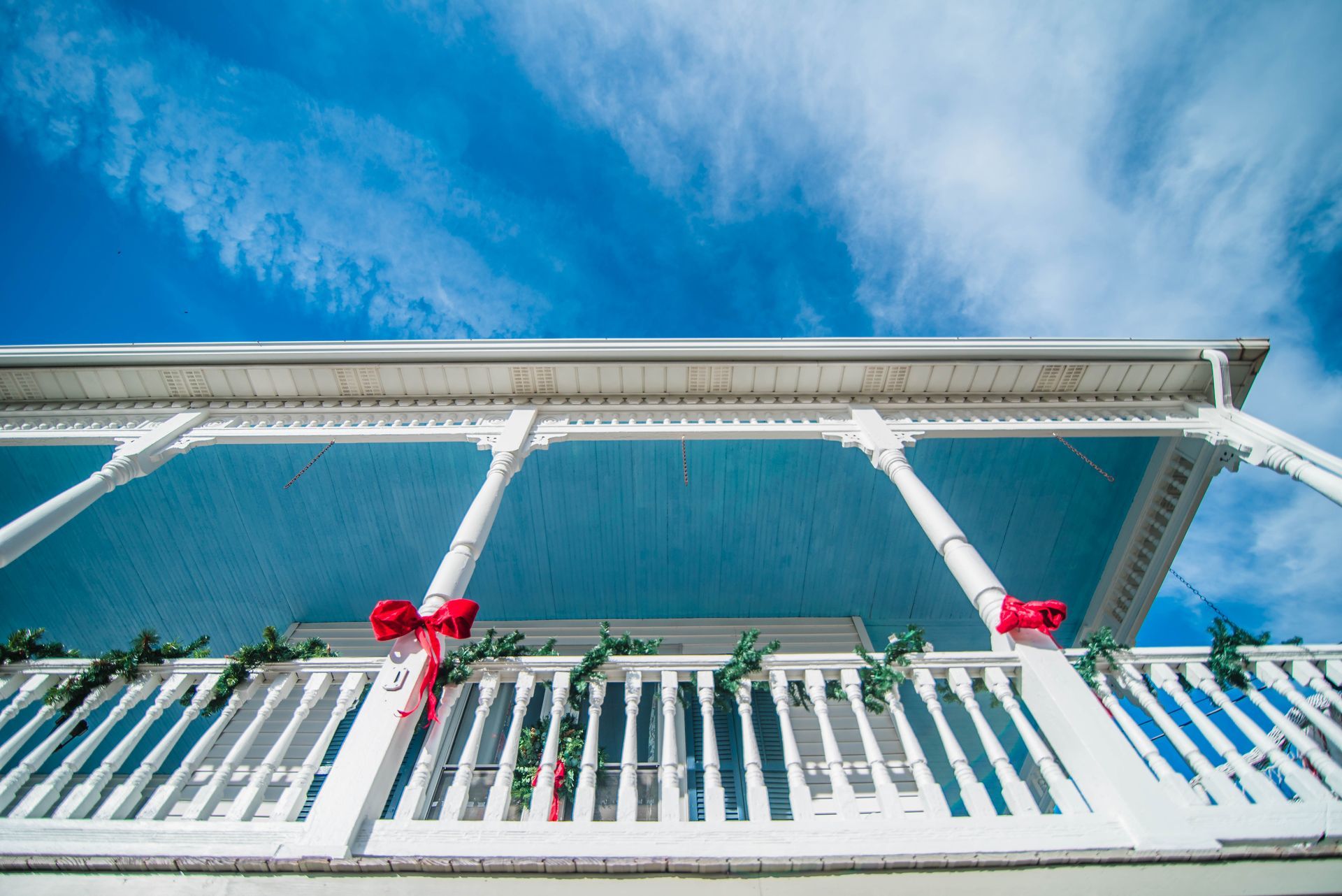 A white house with a balcony decorated for christmas with a red bow.