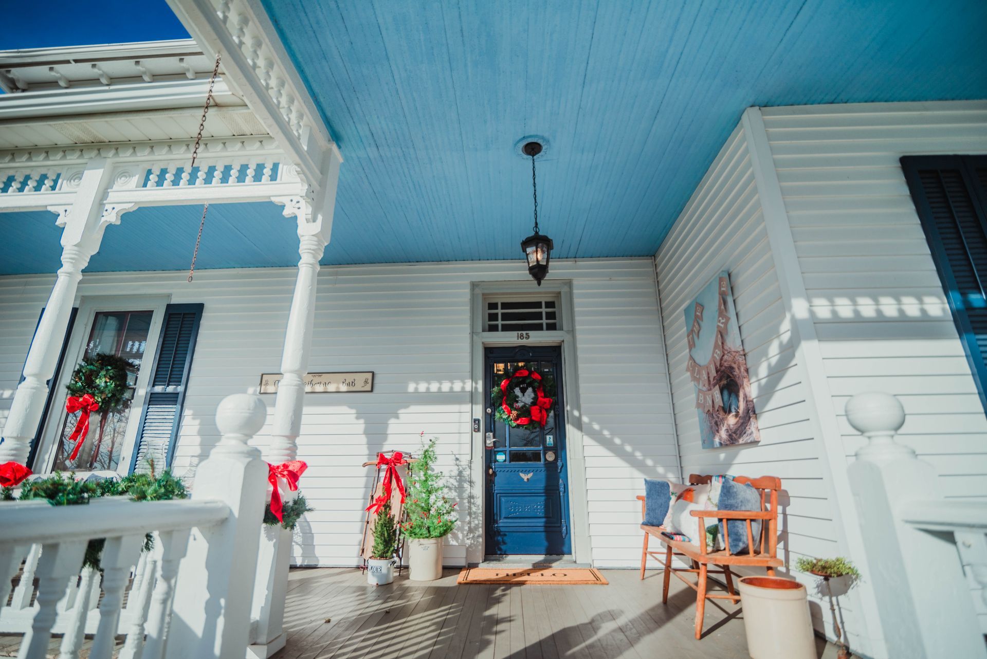 A white house with a blue roof and a porch decorated for christmas.