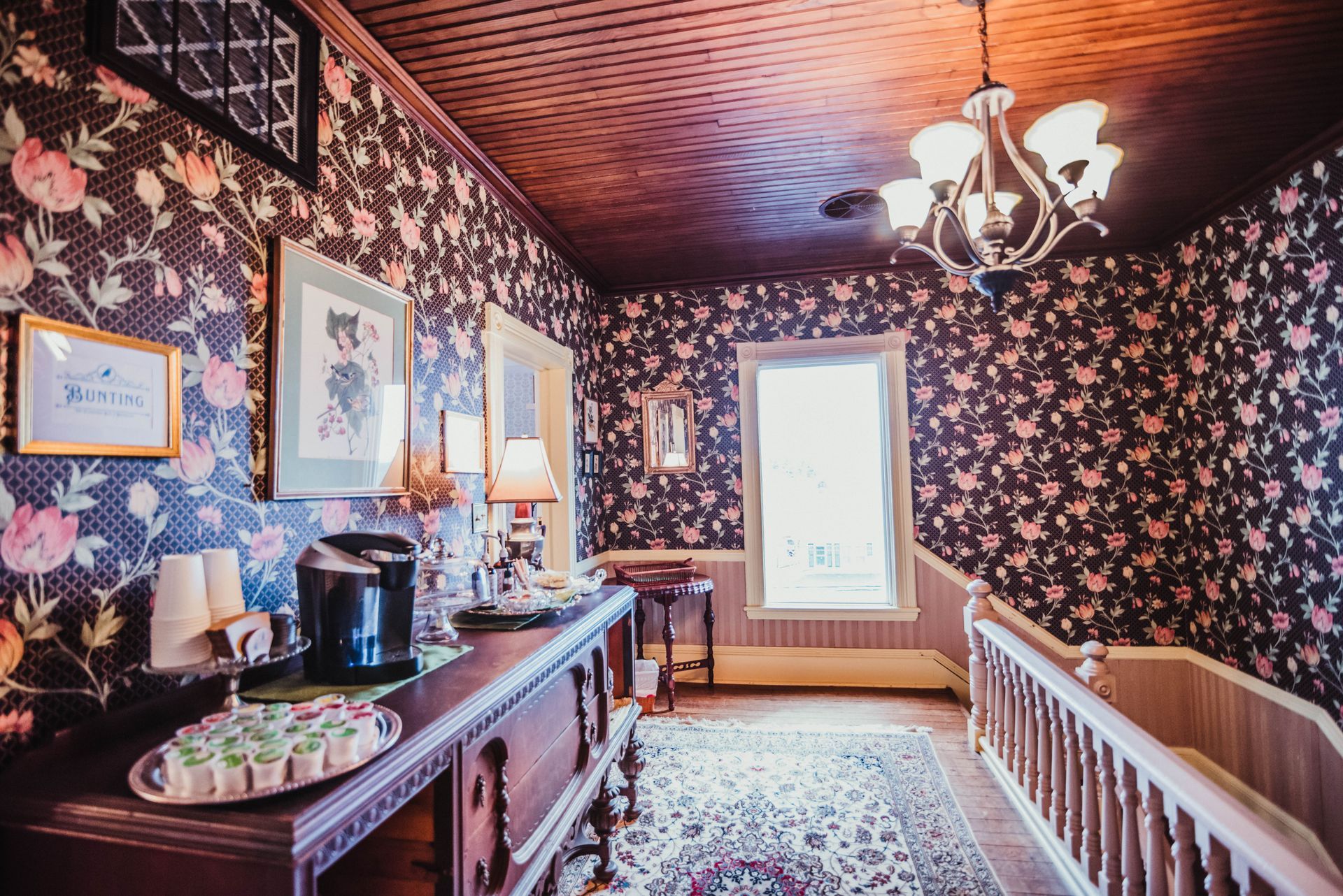 A hallway with a floral wallpaper and a chandelier.