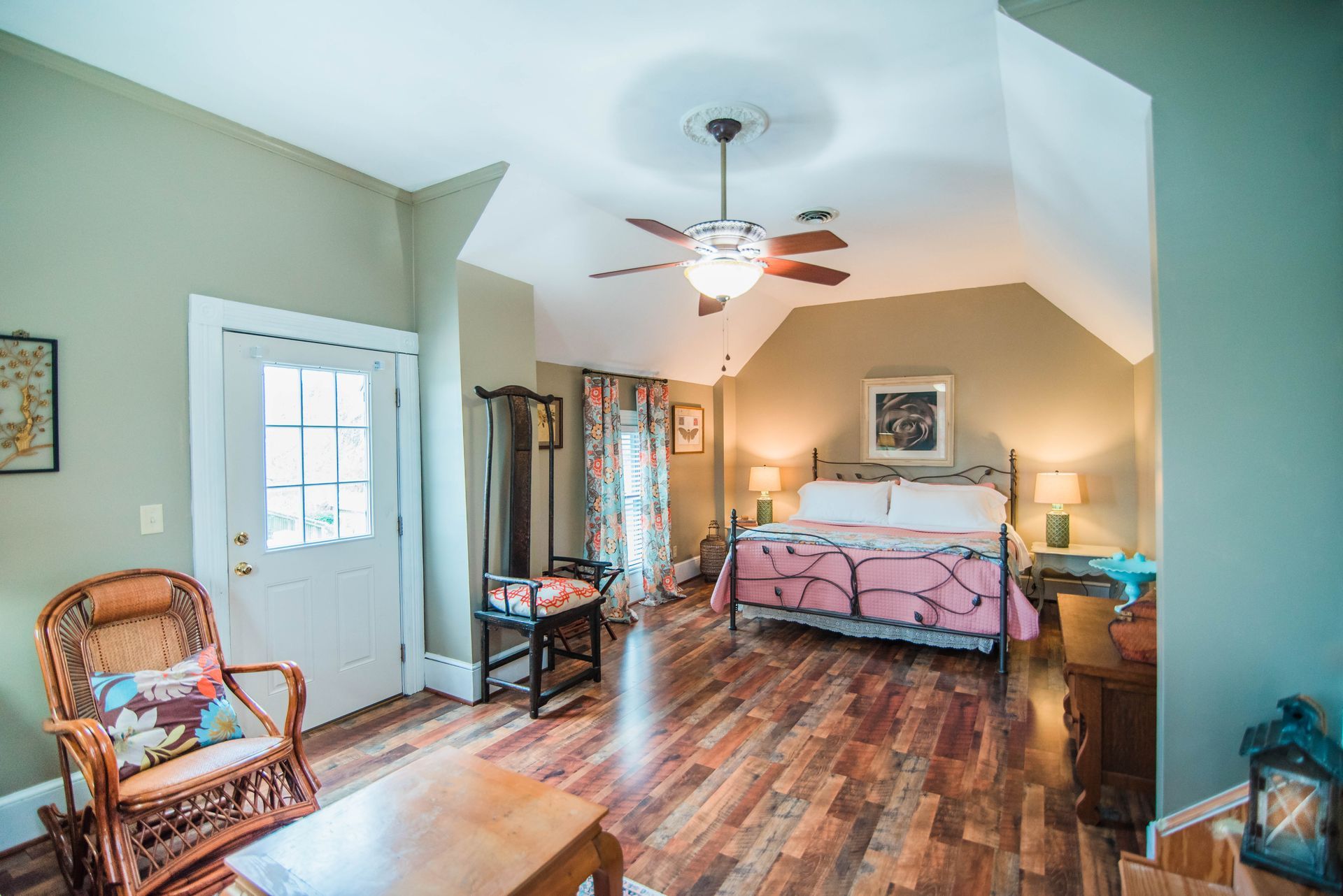 A bedroom with a bed , chair , table and ceiling fan.