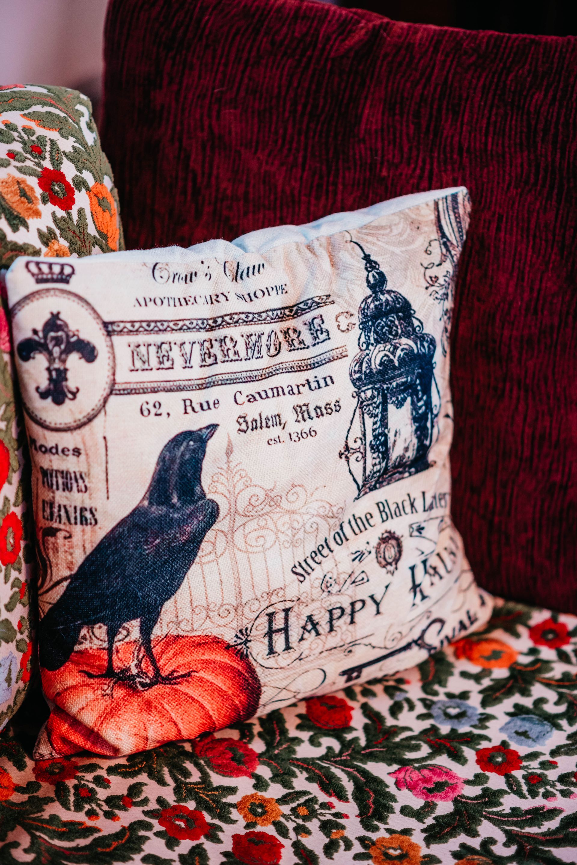 A pillow with a crow and a pumpkin on it is sitting on a couch.