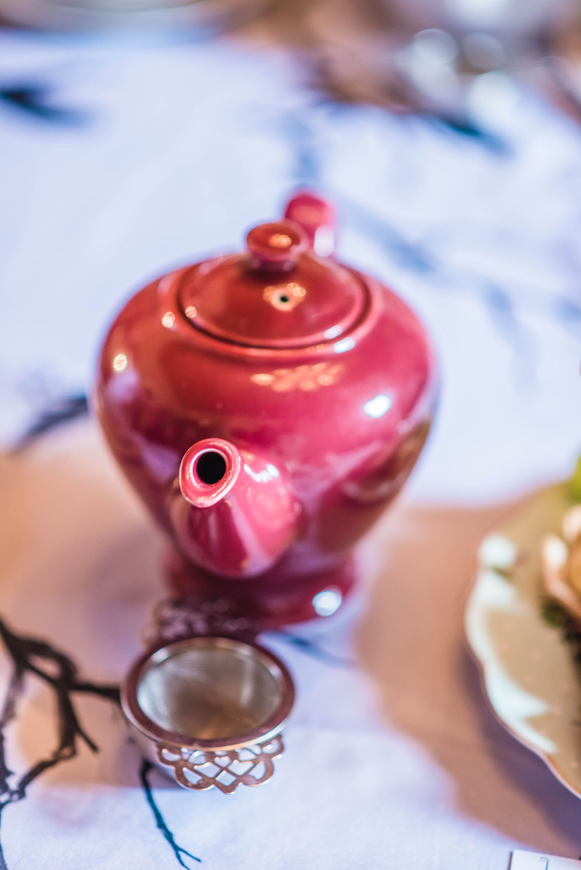 A red teapot is sitting on a table next to a cup.