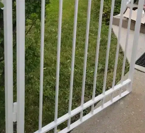 White metal fence beside a grassy yard and concrete walkway