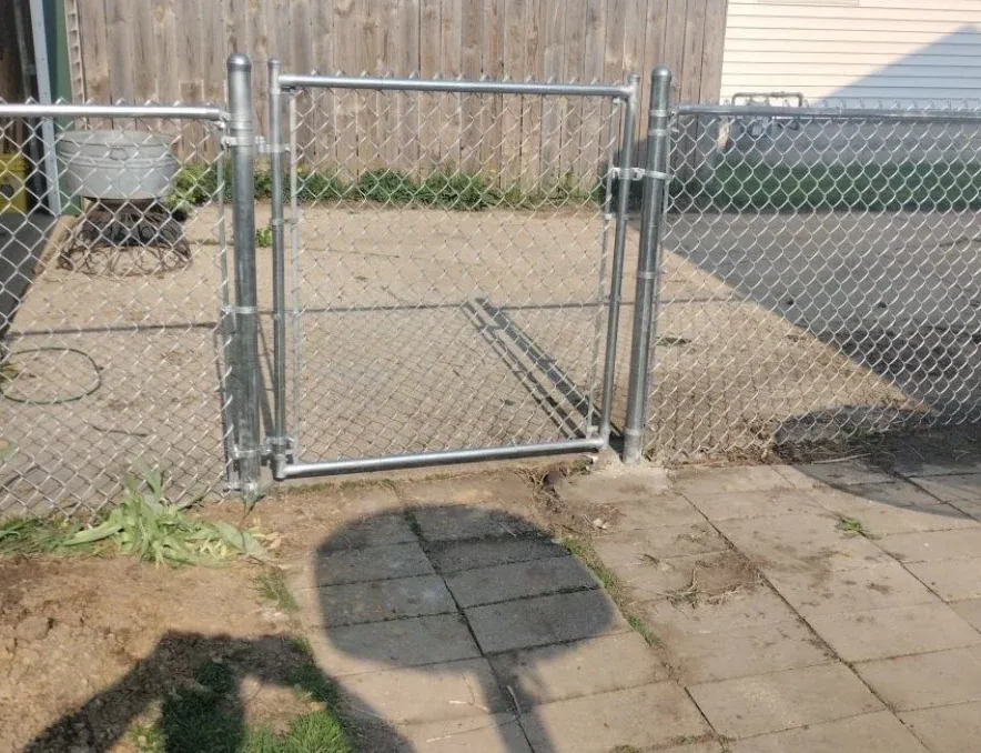 Chain-link gate in a fenced backyard, with a concrete patio and wooden fence behind it.